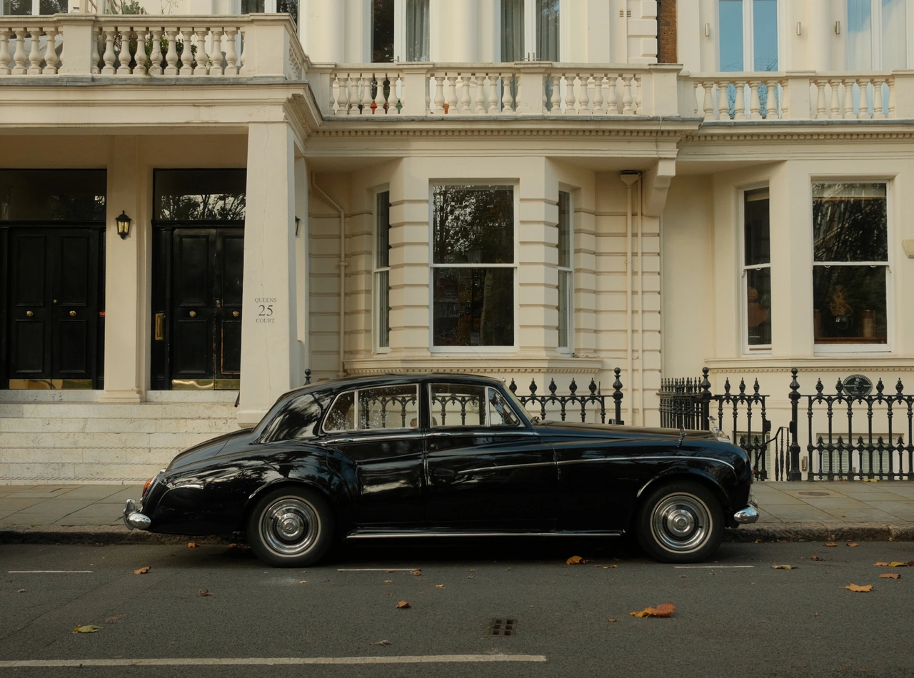 A classic black car outside a cream townhouse