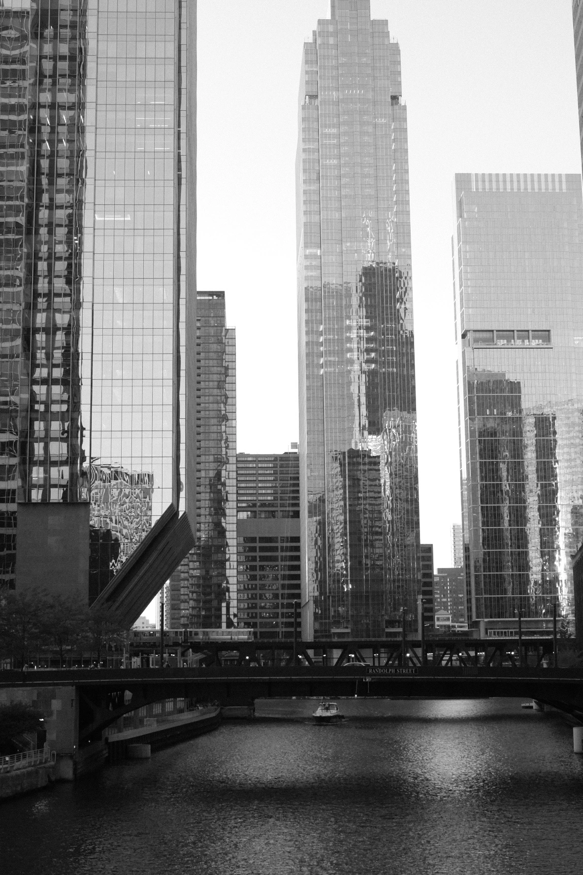 A bridge and stepped skyscraper beside a river, in black and white